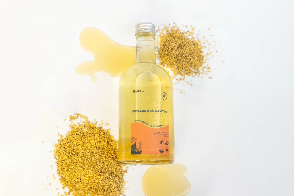Glass bottle of pale yellow oil with a spill and granulated golden grains on a white surface.