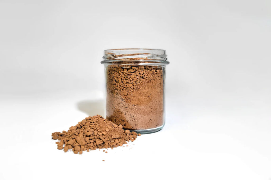 Glass jar filled with cocoa powder, with a small heap spilled in front on a white surface